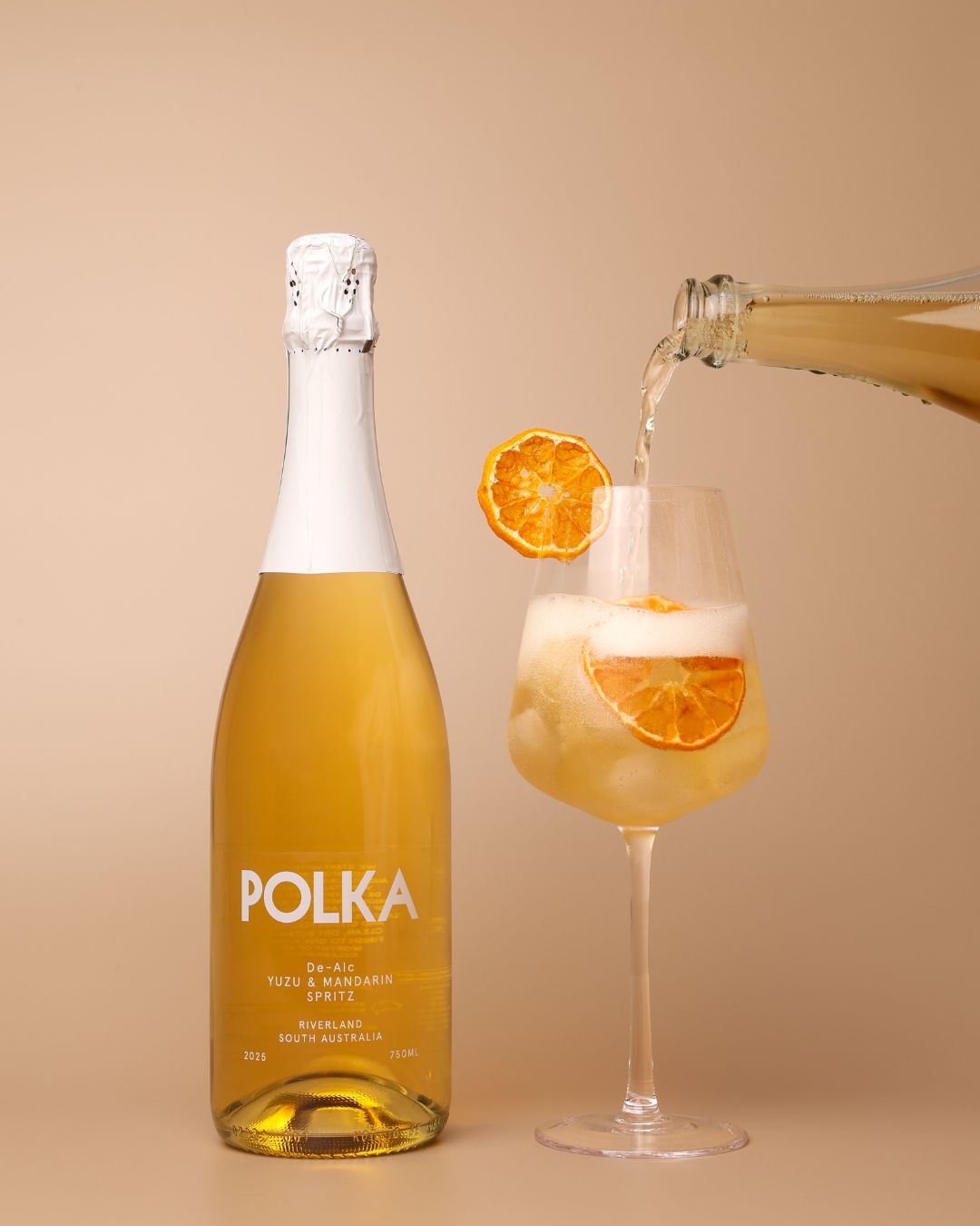 polka non alcoholic yuzu mandarin spritz pouring into glass on plain background