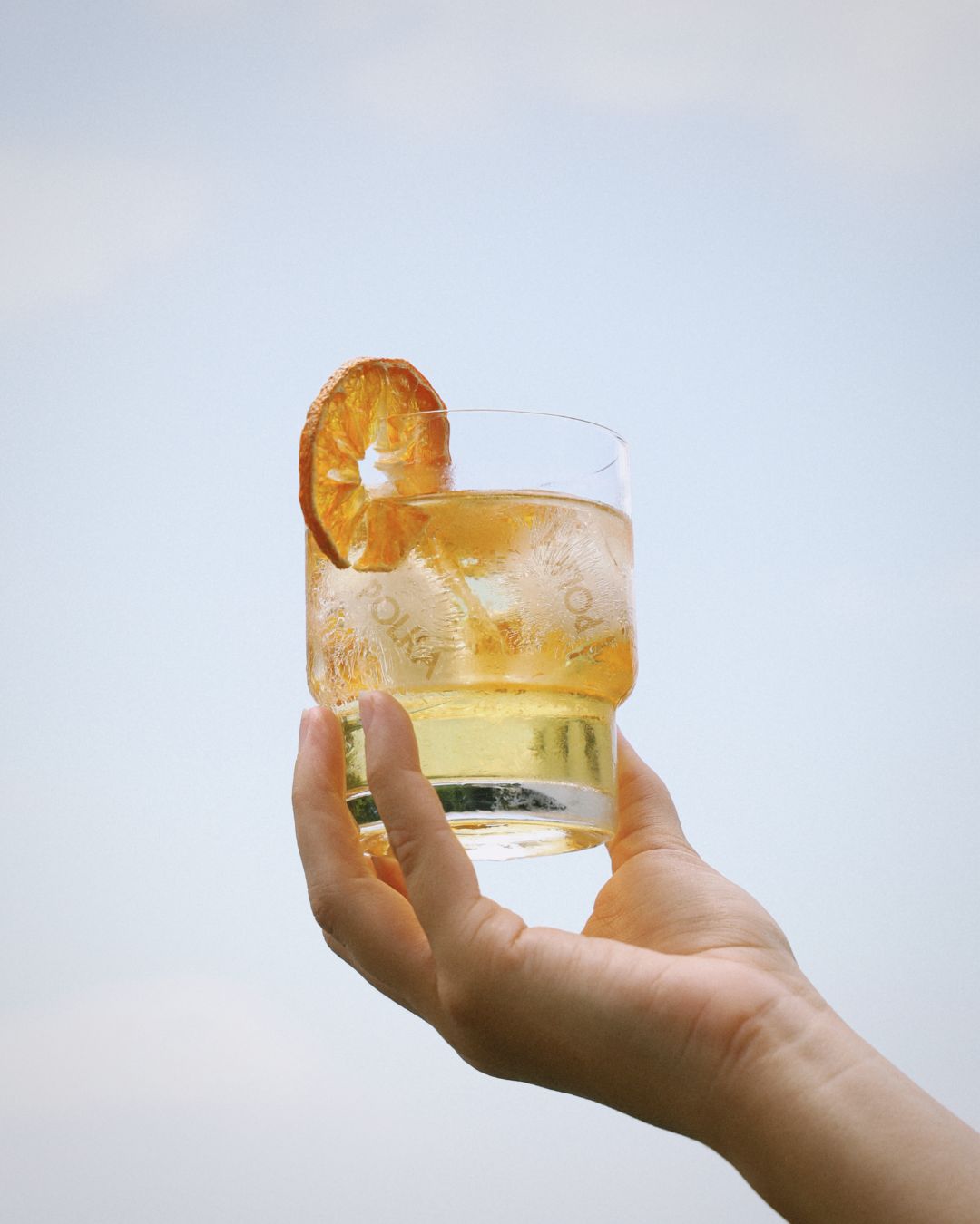 polka yuzu mandarin spritz in glass being held in the air lifestyle shot