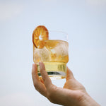 polka yuzu mandarin spritz in glass being held in the air lifestyle shot